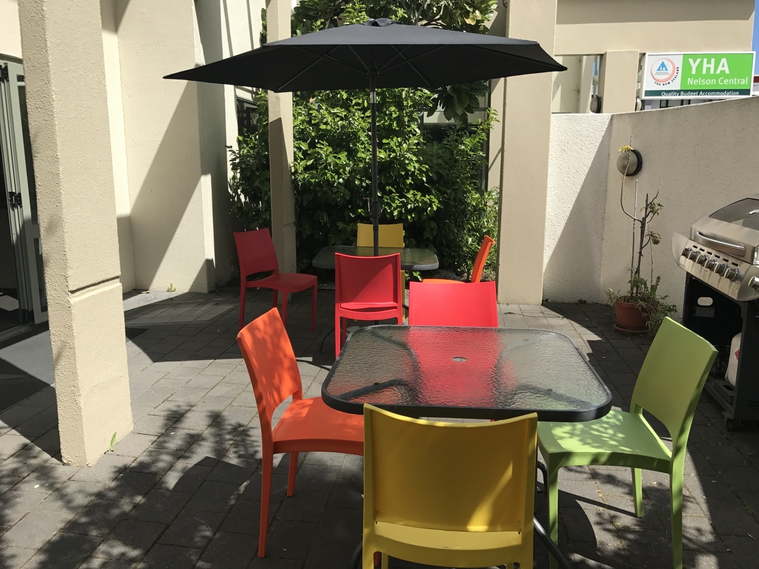 Sunny Courtyard with Bright coloured Chairs, sun umbrella and Free BBQ for cooking at our Nelson Hostel