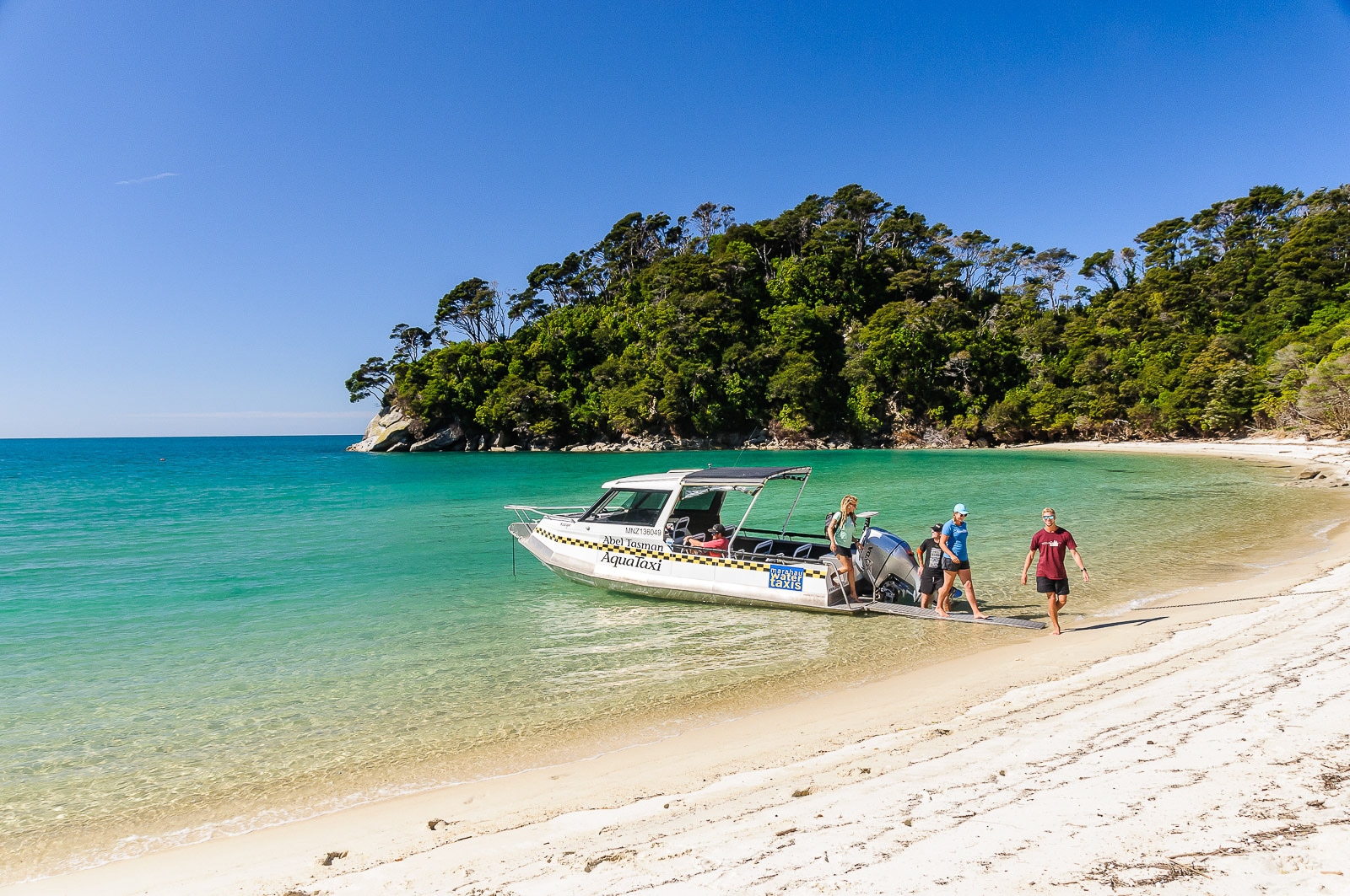 abel-tasman-aqua-taxi Aqua-taxi shuttle offloading travelers onto a golden beach in Abel Tasman National Park, New Zealand, with clear waters and forested coastline in the background